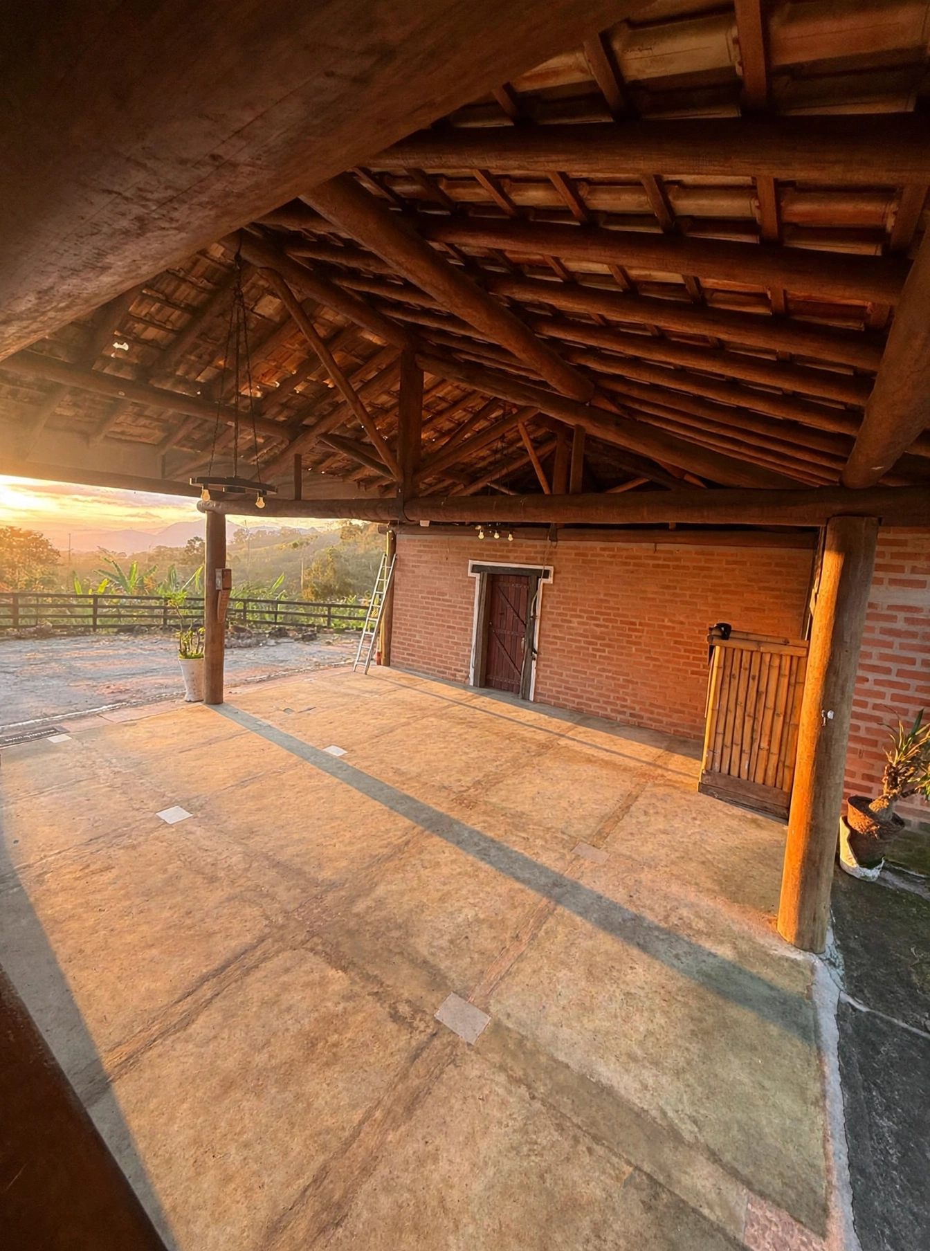 Vista geral do salão aberto, com estrutura de bambu do telhado e parede de tijolo